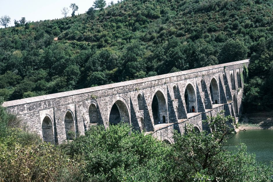 Historic stone aqueduct surrounded by lush greenery under a clear sky.