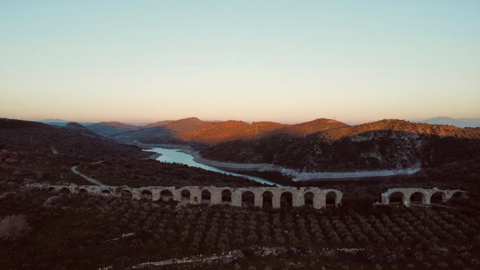 Aerial view of an ancient aqueduct crossing a scenic river valley during a peaceful sunset.