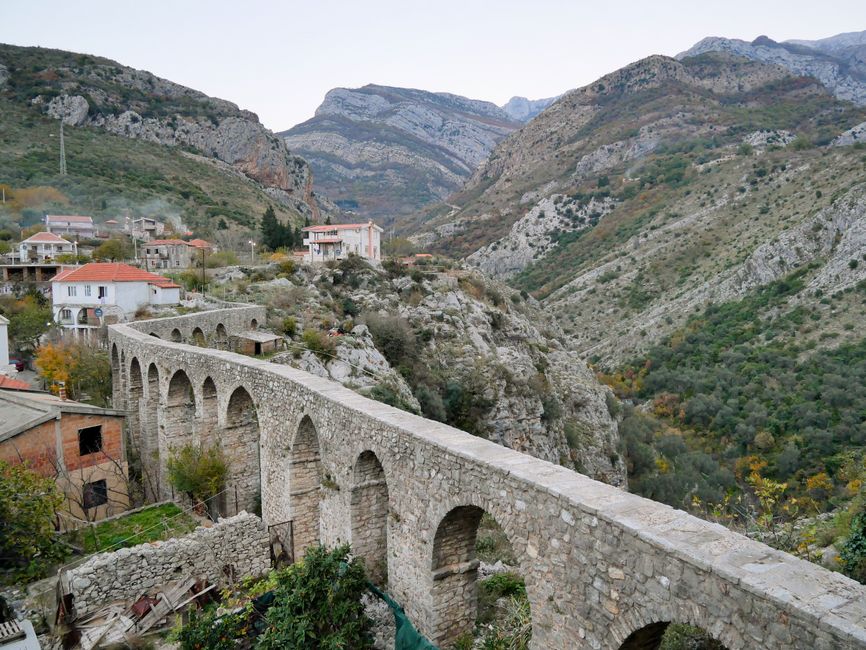 A scenic view of an ancient stone aqueduct in Montenegro, surrounded by lush mountainous terrain.